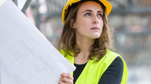 Eine Frau mit Bauhelm hält eine Zeichnung auf einer Baustelle
