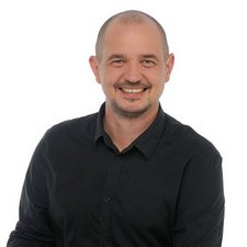 Professionelles Porträt eines freundlichen Mannes mit Glatze Mit einem selbstbewussten Lächeln präsentiert sich der Mann in einem schwarzen Oberteil vor einem hellen Hintergrund.